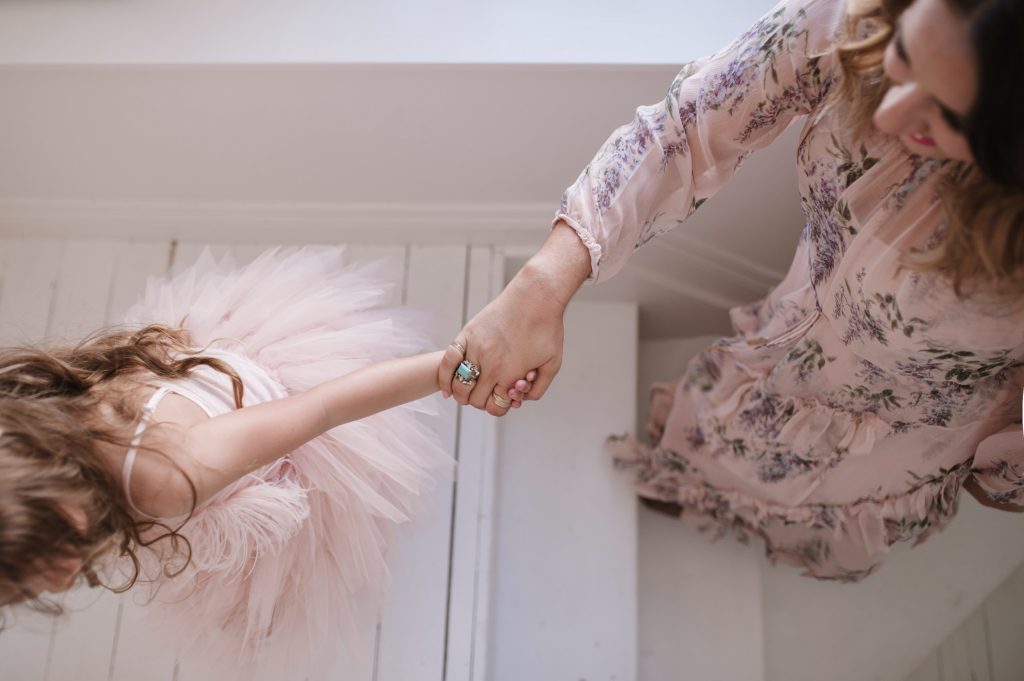 A photo of Clarissa Grace of Waking Up In Paris ascending a white staircase while holding her daughter's tiny hand as she walks ahead of her. Her daughter is wearing a soft pink tutu skirt and Clarissa is in a soft pink floral print dress.