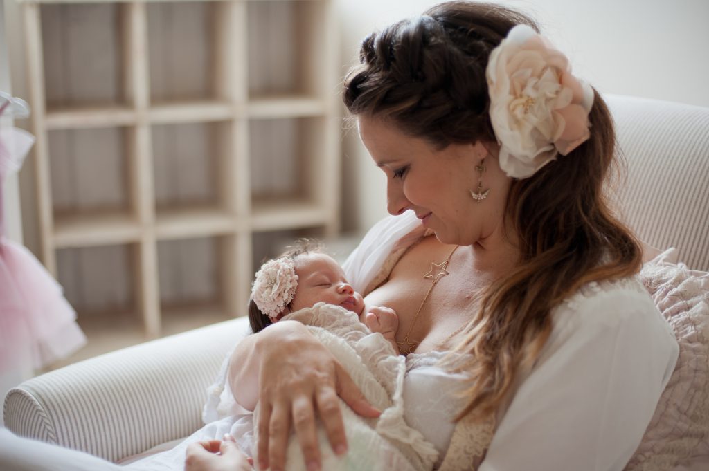 A photo of Clarissa Grace of Waking Up in Paris holding her infant daughter in her arms. She is gazing at her little girl, who is sleeping against her breast. 